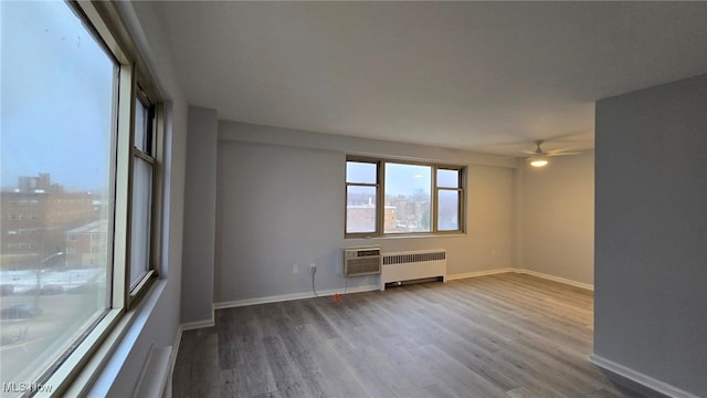 empty room with ceiling fan, wood-type flooring, radiator, and a wall mounted air conditioner