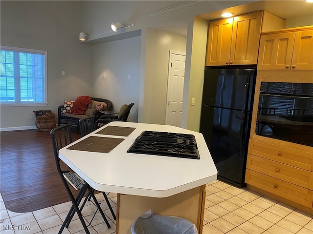 kitchen with light tile patterned floors, a kitchen breakfast bar, black appliances, and a center island