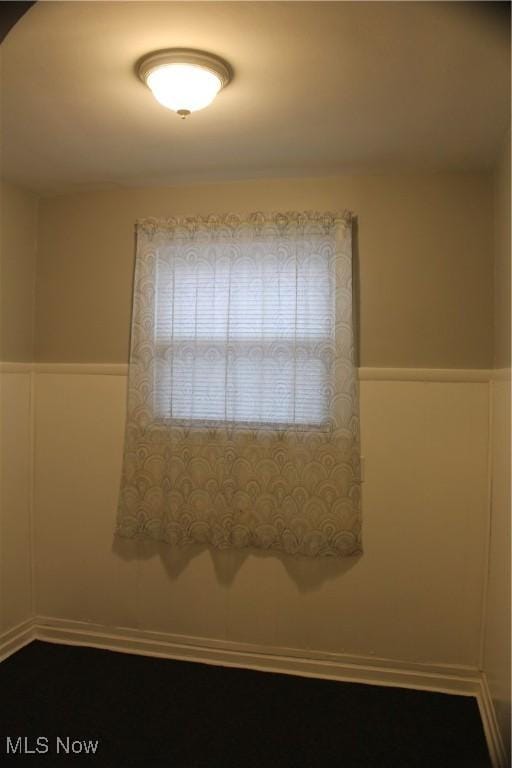 unfurnished room featuring a wainscoted wall