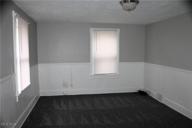 unfurnished room with dark colored carpet, visible vents, and wainscoting