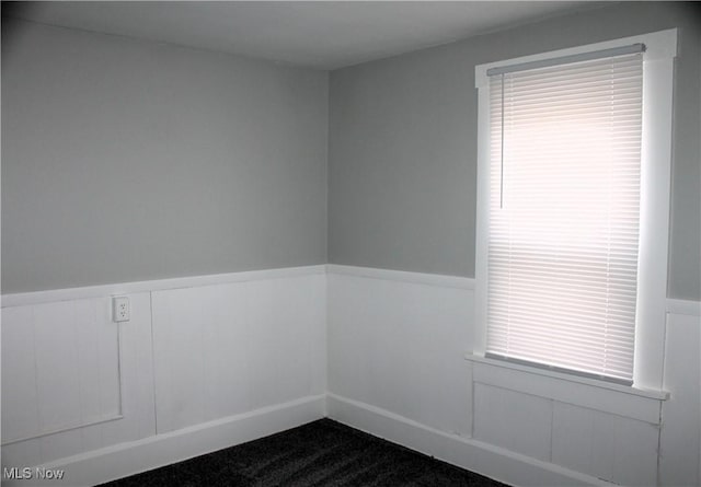 spare room featuring a wainscoted wall, a healthy amount of sunlight, and dark colored carpet