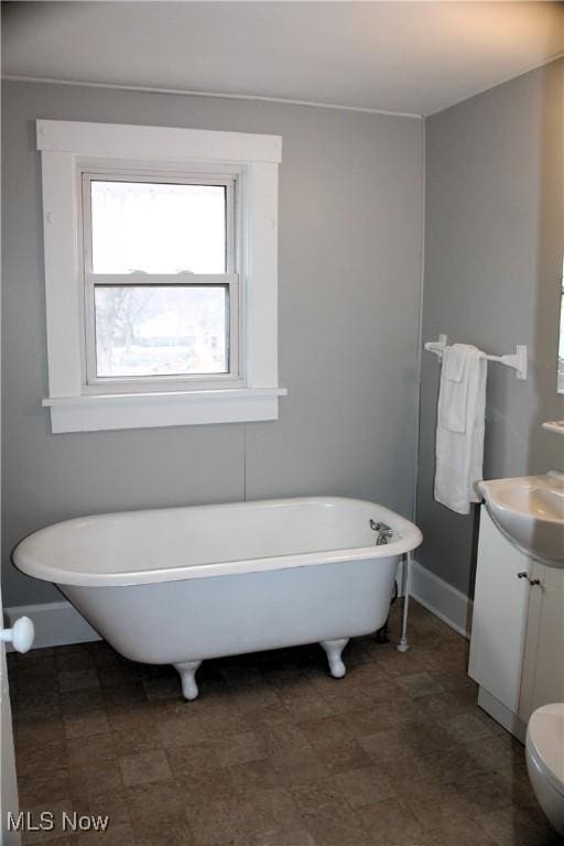 full bathroom with a soaking tub, toilet, vanity, and baseboards