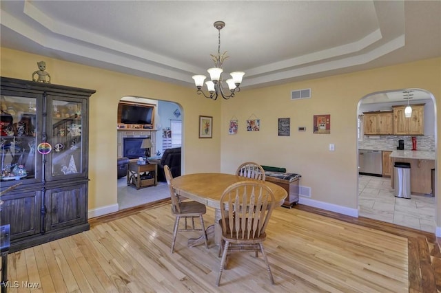 dining area with a notable chandelier, light hardwood / wood-style floors, and a raised ceiling