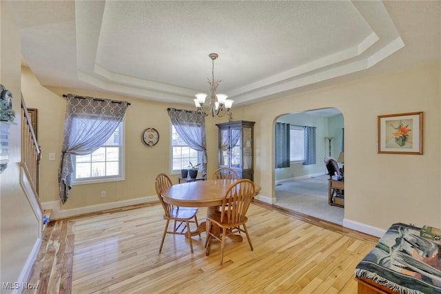 dining room with light hardwood / wood-style floors, a tray ceiling, and a notable chandelier