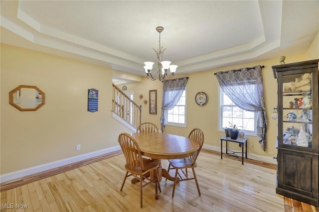 dining space with light hardwood / wood-style floors, an inviting chandelier, and a tray ceiling