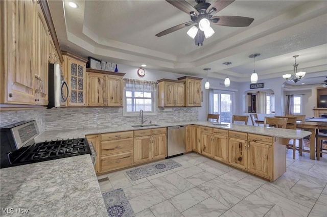 kitchen with kitchen peninsula, stainless steel appliances, decorative light fixtures, sink, and a raised ceiling