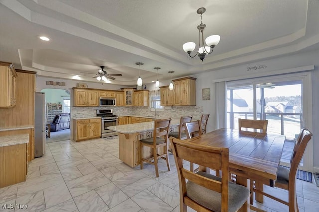 kitchen featuring kitchen peninsula, stainless steel appliances, a raised ceiling, decorative backsplash, and pendant lighting