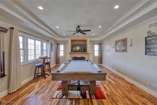 rec room with a raised ceiling, light hardwood / wood-style flooring, billiards, and a textured ceiling