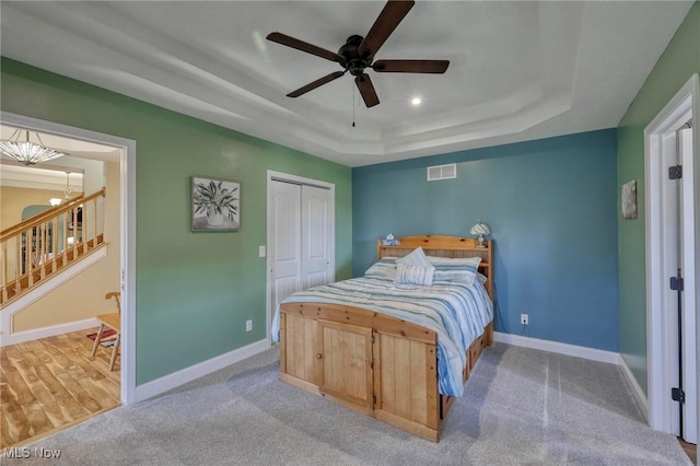 carpeted bedroom featuring connected bathroom, a closet, a tray ceiling, and ceiling fan with notable chandelier