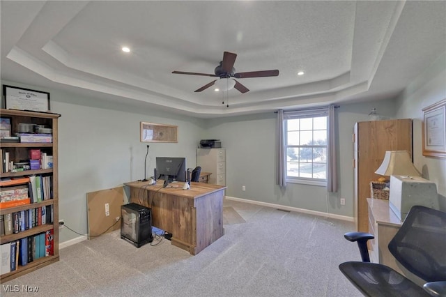 carpeted home office with a tray ceiling and ceiling fan