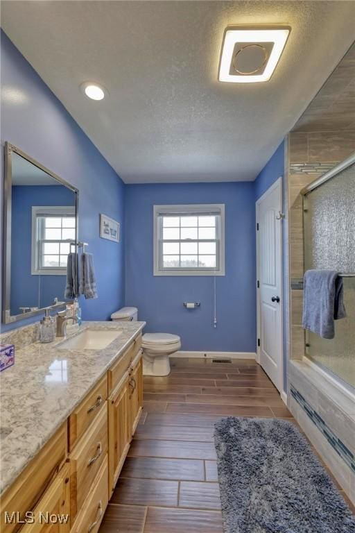 bathroom featuring a textured ceiling, toilet, vanity, and an enclosed shower