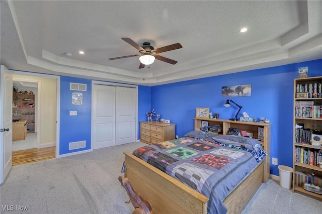 carpeted bedroom with a tray ceiling, ceiling fan, a textured ceiling, and a closet