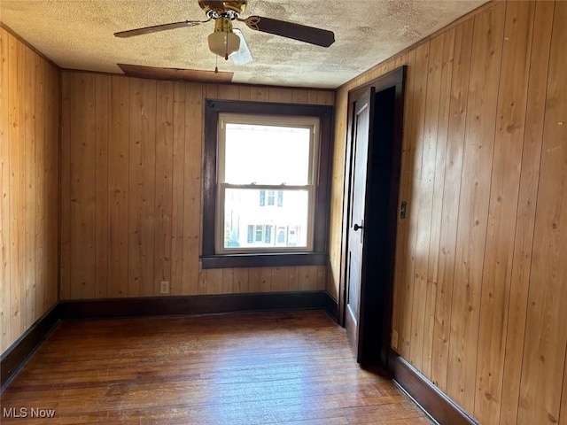 spare room with hardwood / wood-style floors, wood walls, a textured ceiling, and ceiling fan