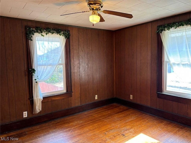 unfurnished room with wood-type flooring, ceiling fan, and wood walls