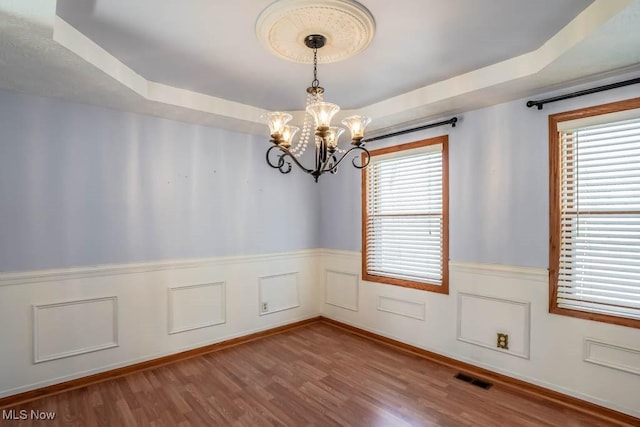 unfurnished dining area featuring wood-type flooring, a chandelier, a raised ceiling, and a wealth of natural light