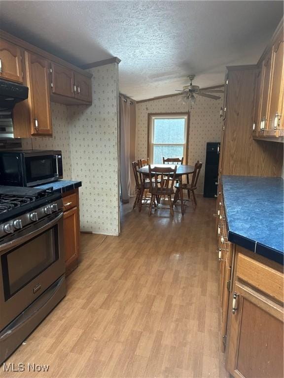 kitchen with tile countertops, light wood-type flooring, ceiling fan, stainless steel appliances, and a textured ceiling