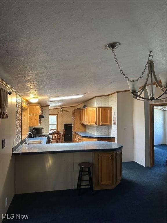 kitchen with sink, kitchen peninsula, dark carpet, and a textured ceiling