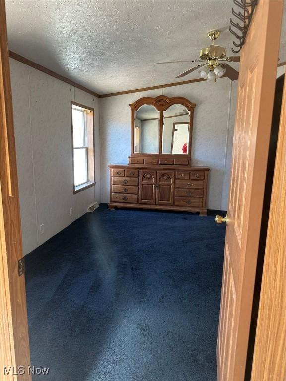 unfurnished bedroom featuring crown molding, a textured ceiling, and dark colored carpet