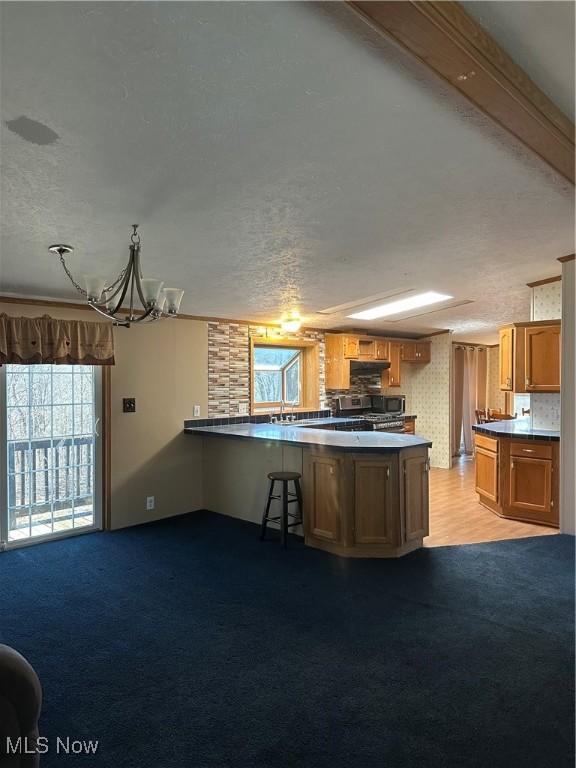 kitchen with stainless steel range oven, sink, a textured ceiling, kitchen peninsula, and light colored carpet