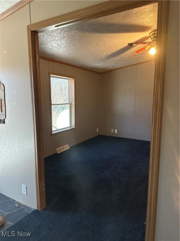 unfurnished room featuring ceiling fan, a textured ceiling, and dark colored carpet