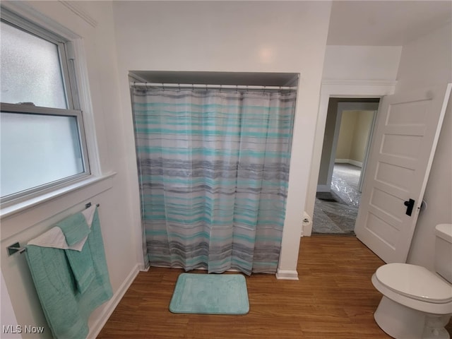 bathroom featuring toilet, a shower with curtain, baseboards, and wood finished floors