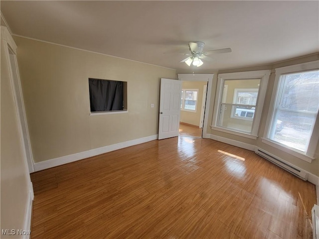 spare room with a healthy amount of sunlight, a baseboard heating unit, ceiling fan, and light hardwood / wood-style flooring