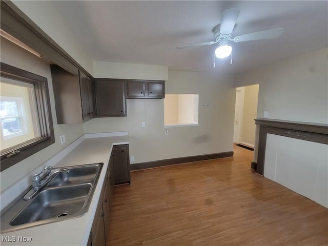 kitchen featuring light countertops, a sink, dark brown cabinetry, light wood-type flooring, and baseboards