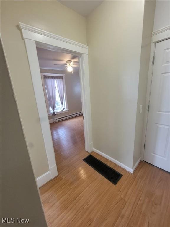 corridor featuring a baseboard heating unit, light wood-type flooring, visible vents, and baseboards