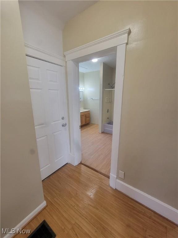 hall featuring visible vents, light wood-style flooring, and baseboards