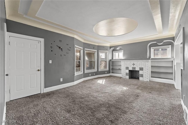 unfurnished living room featuring ornamental molding, a brick fireplace, carpet flooring, and a tray ceiling