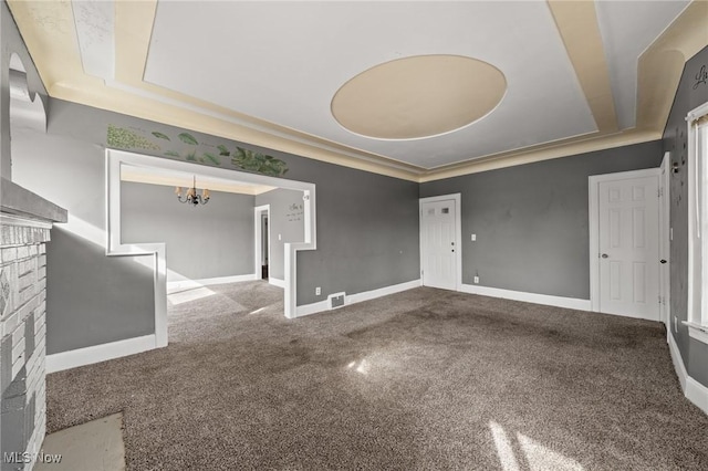 unfurnished living room with crown molding, a tray ceiling, a chandelier, and carpet