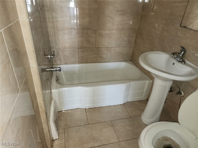 bathroom featuring tiled shower / bath, toilet, tile patterned flooring, and tile walls