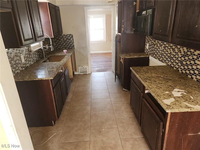 kitchen featuring dark brown cabinetry, sink, light stone counters, tasteful backsplash, and light tile patterned floors