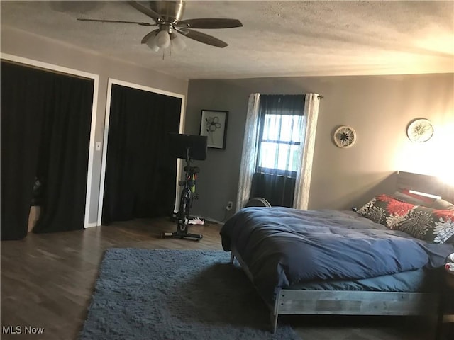 bedroom with multiple closets, dark hardwood / wood-style floors, a textured ceiling, and ceiling fan