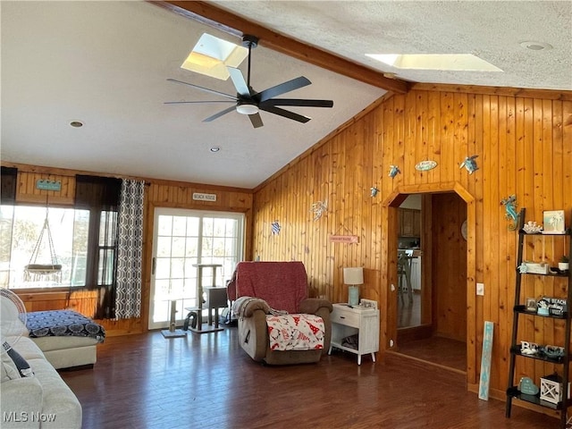 living room featuring vaulted ceiling with skylight, wooden walls, ceiling fan, dark wood-type flooring, and a textured ceiling