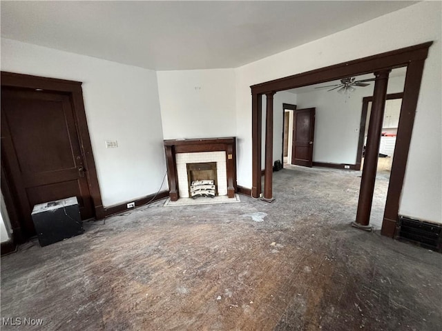 unfurnished living room with ceiling fan, a tiled fireplace, and ornate columns