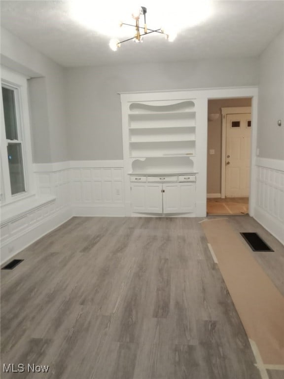 unfurnished dining area with wainscoting, visible vents, an inviting chandelier, and wood finished floors