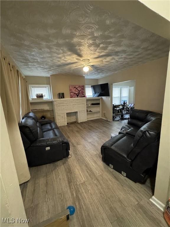 living room with hardwood / wood-style flooring, ceiling fan, a brick fireplace, and a textured ceiling