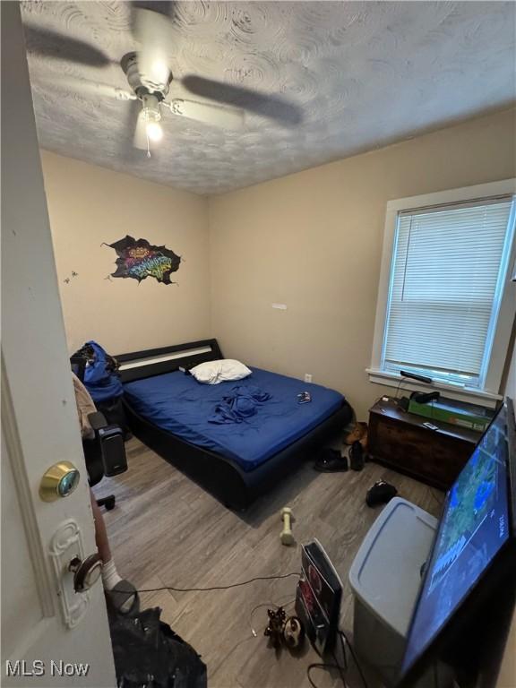 bedroom featuring wood-type flooring, ceiling fan, and a textured ceiling