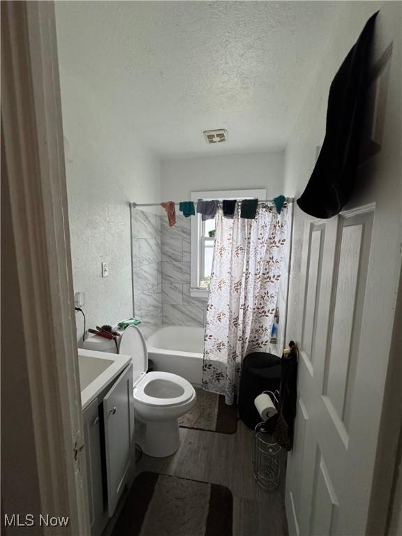 full bathroom with hardwood / wood-style flooring, vanity, shower / tub combo, toilet, and a textured ceiling