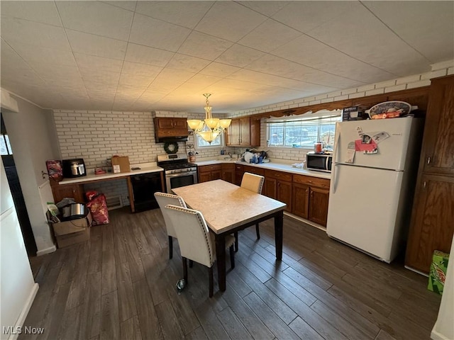 kitchen with dark wood-type flooring, brick wall, appliances with stainless steel finishes, and decorative light fixtures