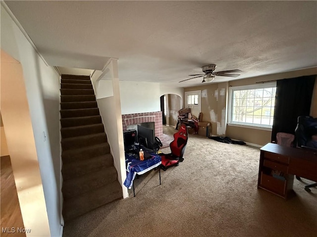 interior space featuring carpet, a textured ceiling, ceiling fan, and a brick fireplace