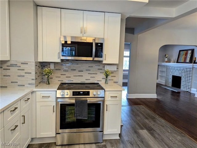 kitchen with stainless steel appliances, white cabinetry, dark wood-type flooring, and a tiled fireplace