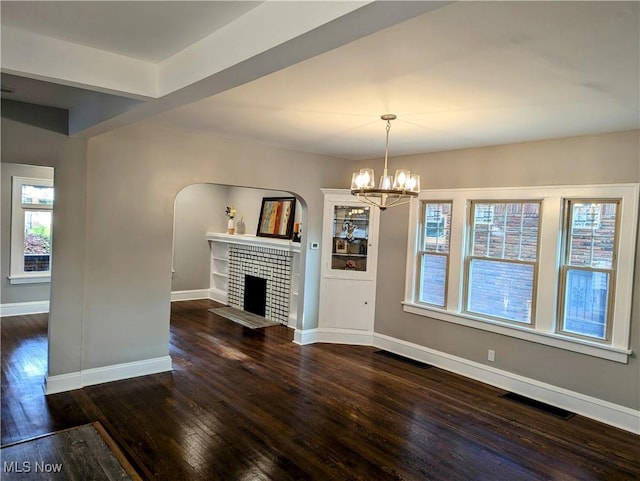 unfurnished living room featuring dark hardwood / wood-style flooring, a brick fireplace, and a chandelier