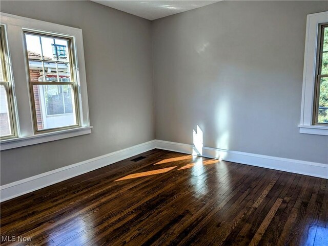 empty room with baseboards, dark wood-style floors, and a healthy amount of sunlight