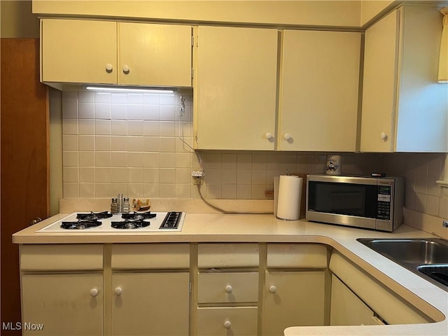 kitchen featuring cream cabinets, white gas stovetop, sink, and backsplash