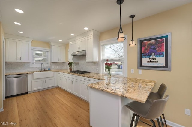 kitchen with a kitchen bar, sink, hanging light fixtures, stainless steel appliances, and white cabinets