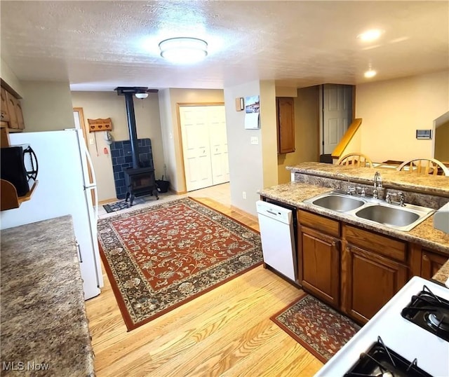 kitchen with sink, white appliances, light hardwood / wood-style flooring, a textured ceiling, and a wood stove