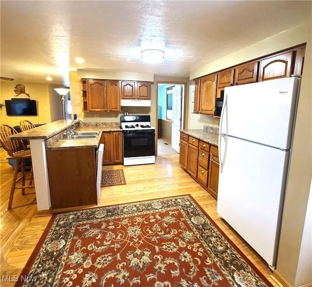 kitchen with a breakfast bar area, white fridge, range, kitchen peninsula, and light hardwood / wood-style flooring