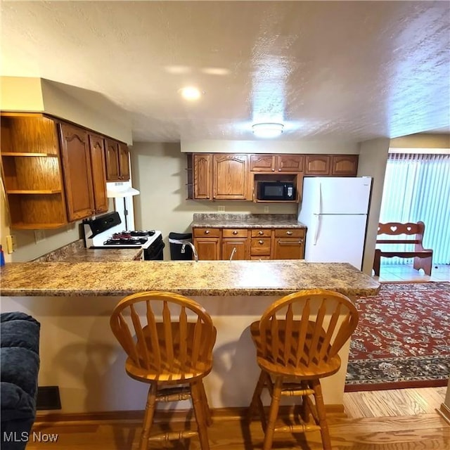 kitchen featuring a breakfast bar, white refrigerator, range, kitchen peninsula, and light stone countertops